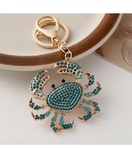 Detail of a golden crab keychain with peacock blue rhinestones on a white surface