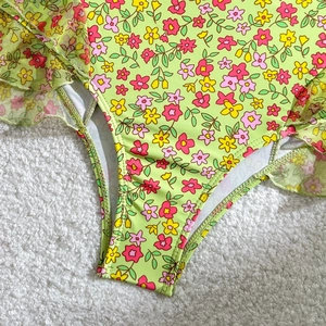 Détail d'un maillot de bain fleuri avec bords en tulle vert clair sur tapis doux