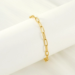 Detailed view of a gold paperclip link chain bracelet on a white cylinder prop