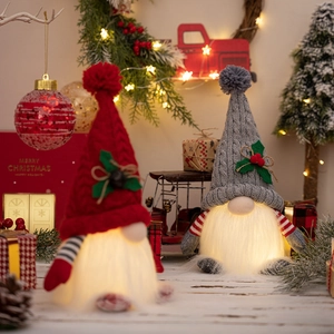 Detail of two Christmas gnomes with glowing bodies and festive knitted hats on white wood