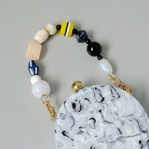 Close-up of colorful acrylic beaded handle on white marble texture luxury handbag