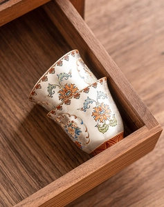 Close-up of stacked silver enamel tea cups with floral patterns in a dark wooden box