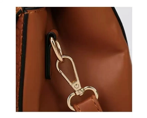Close-up of golden lobster clasp and strap connection on brown leather handbag