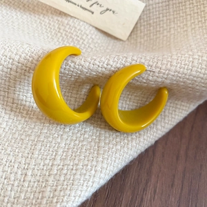 Gros plan de créoles en résine jaune vif en forme de C sur fond de tissu texturé