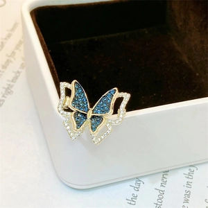 Detailed view of a gold butterfly brooch with blue and clear zircon crystals on a box