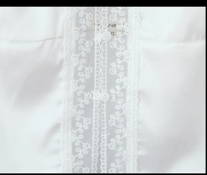 Detailed view of white satin fabric with delicate lace trim and round button accents
