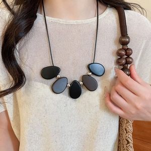 Detail of vintage resin and wood bead pendant necklace worn on textured beige knit top