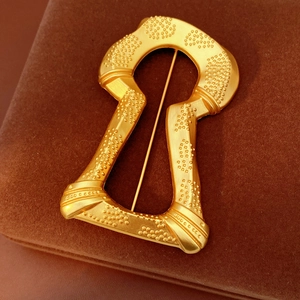 Macro shot of a vintage gold keyhole brooch with embossed texture on brown velvet