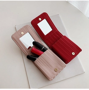 Mini portable leather lipstick pouch with mirror in red and pink colors shown on a book