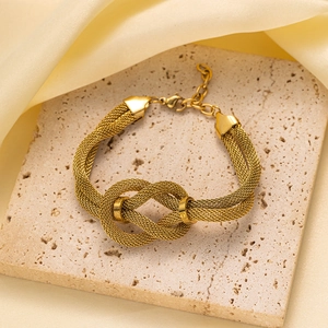 Detalle de la pulsera de malla dorada con un dije central de nudo de infinito