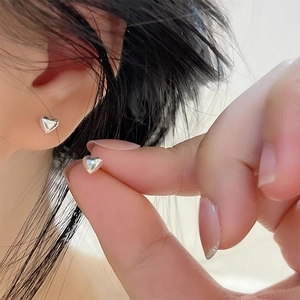 Minimalist S925 sterling silver heart stud earrings shown on finger for scale