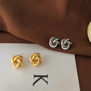 Macro shot of minimalist knotted stud earrings in polished gold and silver metal finishes