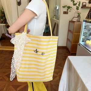 Detail of canvas tote bag showing yellow stripes, butterfly embroidery, and lace bow