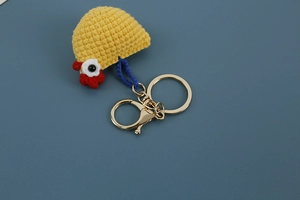 Close-up of a handmade yellow crocheted chick keychain with a gold metal hook