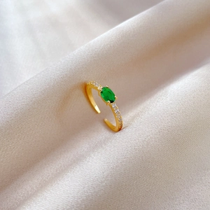 Detail of adjustable gold ring with green oval zircon on premium silk background