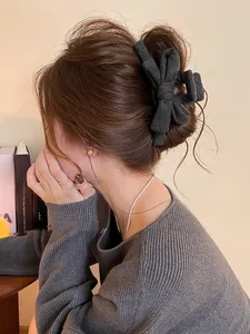 Détail d'une pince à cheveux avec nœud en tissu gris foncé portée par un mannequin