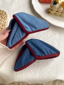 Detail of denim blue triangle hair claw clip with contrast red stitching on white fabric