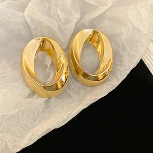 Polished gold oval hollow twisted earrings displayed on white textured tissue paper