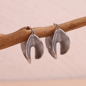 Macro detail of silver layered wave earrings displayed on a rustic branch