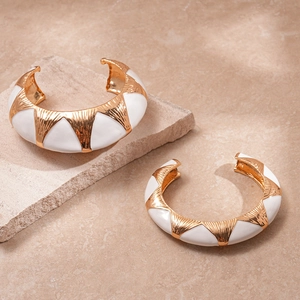 Detail of chunky gold-plated oval cuff featuring white enamel and radial wave texture