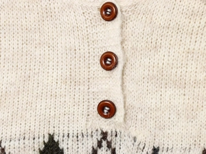 Detailed close-up of cream knit cardigan with amber buttons and jacquard pattern