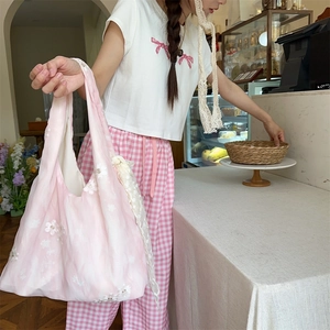 Close-up of pink lace tote bag with white 3D floral accents in a cozy cafe setting