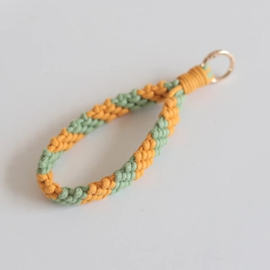 Close-up of handmade yellow and green woven cotton wristlet strap with gold metal ring