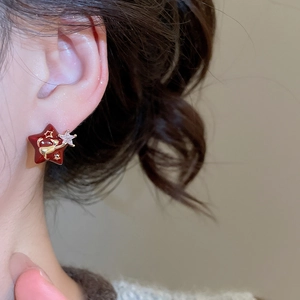 Detail of red star earring with gold cat pattern and sparkling stone inlay on a model