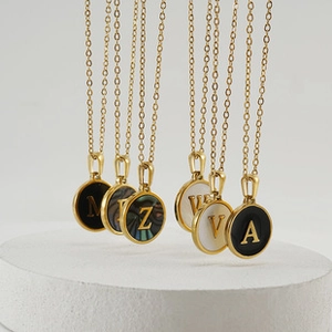 Detail of round gold pendant necklace with letter inlay and mother of pearl texture