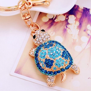 Macro shot of gold turtle keychain with blue and white crystals on floral background