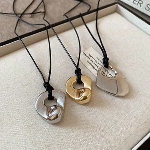 Detail of three hollow heart pendants in gold and silver finish on black cord chains