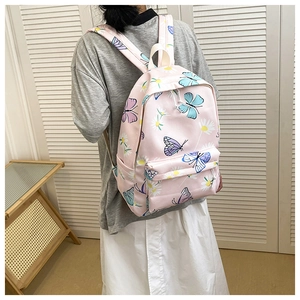 Pink canvas backpack with butterfly print worn by model from a side-rear perspective