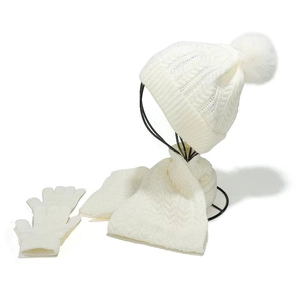 Nahaufnahme des weißen Zopfstrick-Wintersets mit Bommelmütze, Schal und Handschuhen