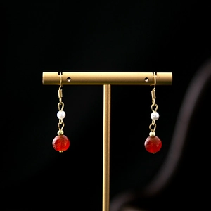 Detail of red agate beads and white pearl earrings on a golden T-shaped display stand