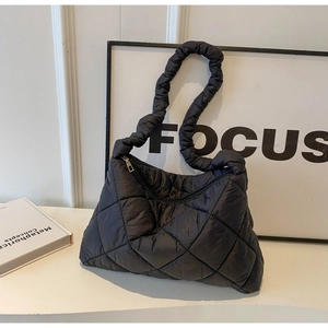 Detailed view of black quilted down shoulder bag with zipper on a minimalist white stand