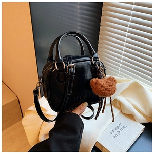 Detail shot of a black patent leather crossbody bag with a plush bear charm on white fabric
