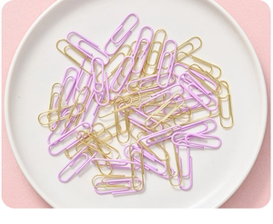 Close-up of pastel purple and gold paper clips in a white dish for office stationery