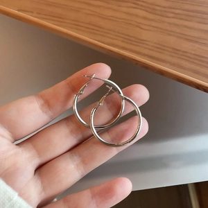 Polished silver hoop earrings held by hand showing medium circular size and classic style