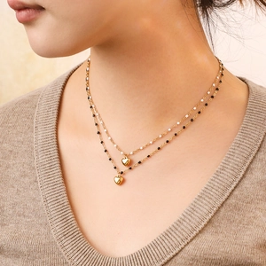 Détail d'un collier doré à deux rangs avec perles blanches et pendentif en cœur