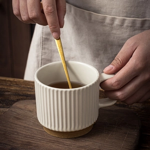 Off-white ceramic coffee mug with vertical stripes and gold spoon on a wooden table