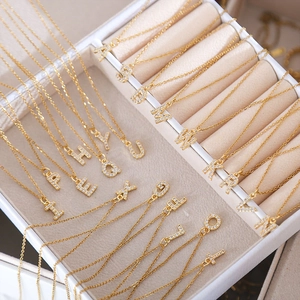 Macro shot of gold square letter pendants with zircon inlay on a white jewelry display box