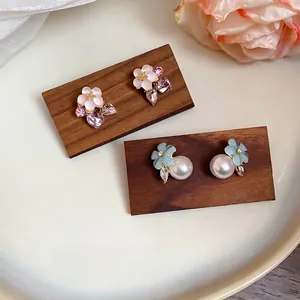 Floral stud earrings with pearls and crystals in pink and blue on a wooden stand