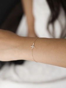 Close-up of gold cross bracelet with white zircon inlay worn on a female wrist