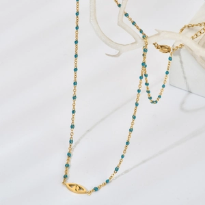 Détail du collier œil maléfique doré avec perles bleues sur un support décoratif blanc