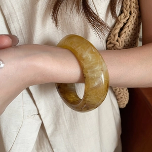 Macro detail of amber marble pattern on a wide resin bangle worn on a wrist