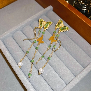 Close-up of gold butterfly tassel earrings with emerald green zircon and white pearl details