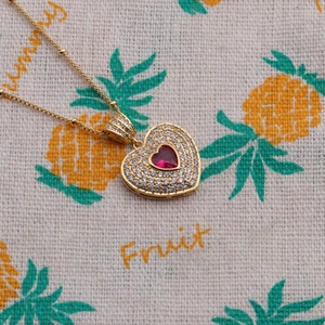 Detailed macro shot of a gold heart necklace with red gemstone and clear zircon accents