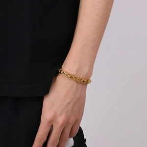 Gros plan d'un bracelet gourmette byzantin doré pour homme porté au poignet du mannequin