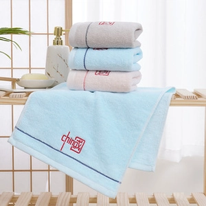 Detail of soft coral fleece towels with fruit embroidery on a rustic bathroom shelf