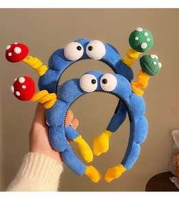 Dettaglio del cerchietto in peluche blu con occhi a cartone e decorazioni a fungo